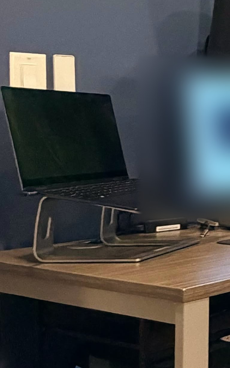 The laptop on its stand at the far left of the desk